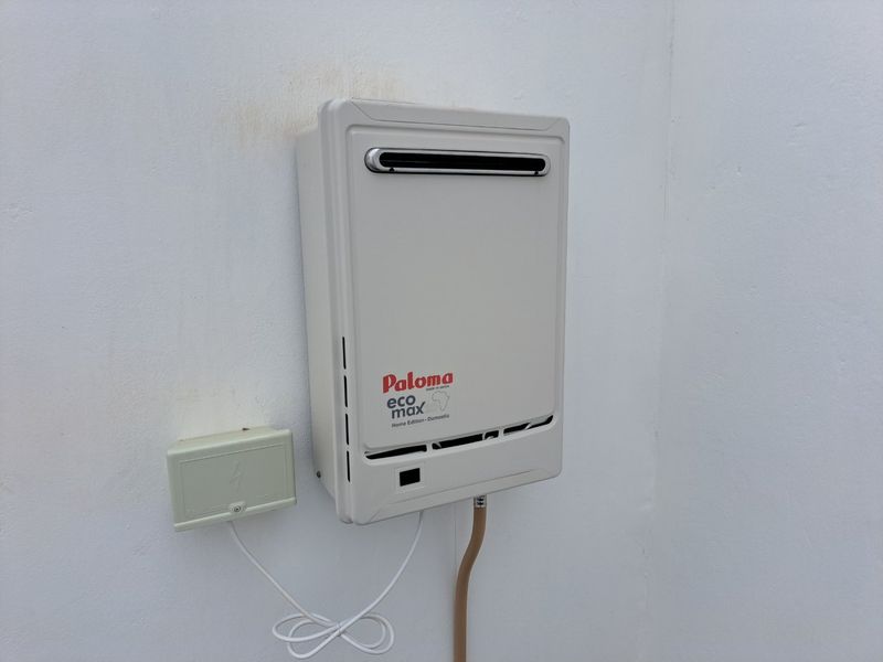 Wall-mounted gas water heater unit installed on an exterior wall, featuring a clean and functional setup.
