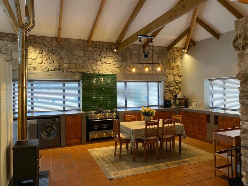 Spacious open-plan kitchen and dining area featuring exposed timber beams, stone feature walls, terracotta flooring, and a built-in wood-burning fireplace.