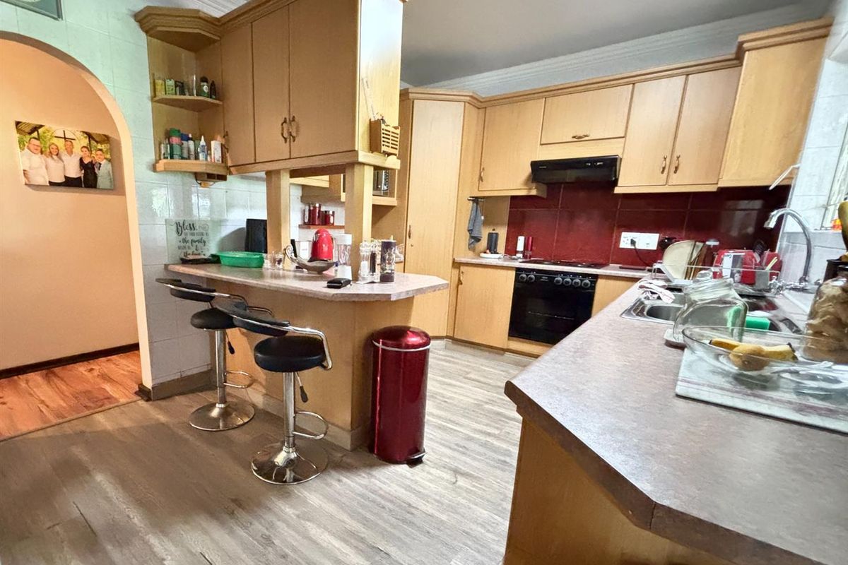 A functional kitchen featuring light wood cabinetry, a breakfast bar, integrated oven, extractor fan, and tiled splashbacks.