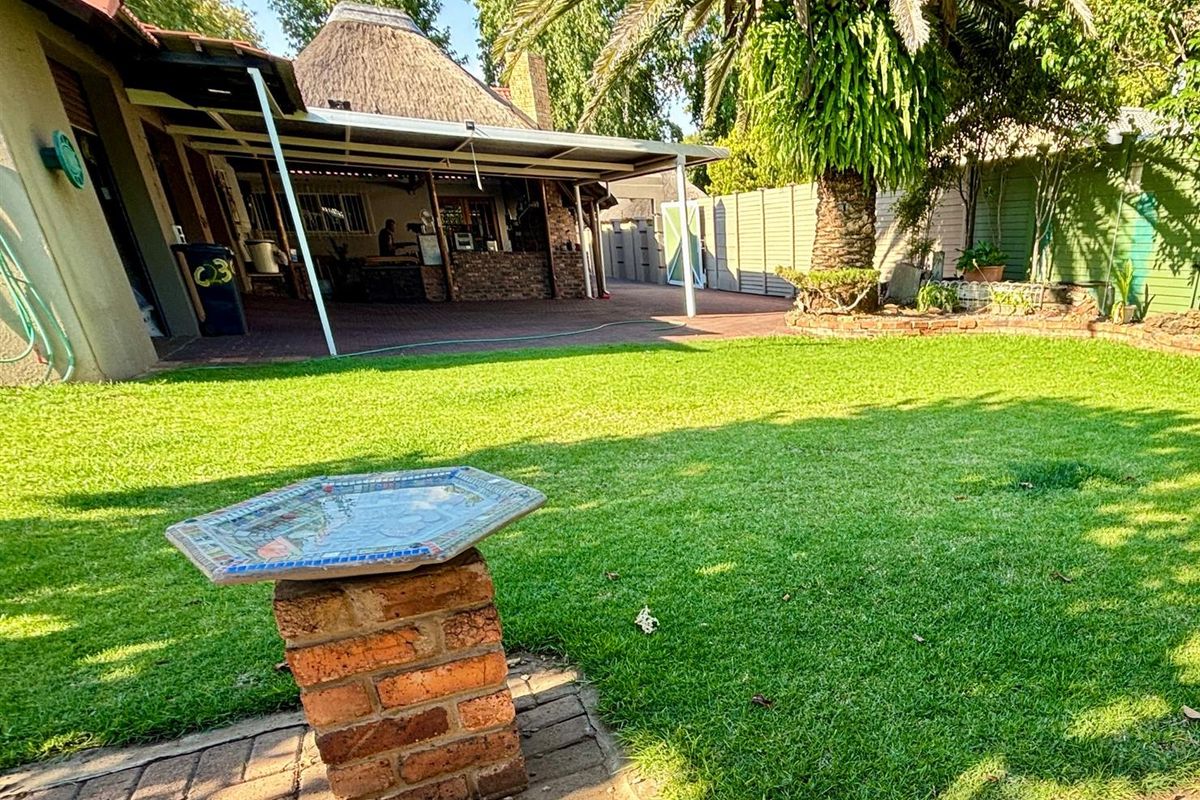 A spacious rear garden featuring a well-maintained lawn, a brick-paved patio area, and a covered outdoor entertainment space with a thatched roof.