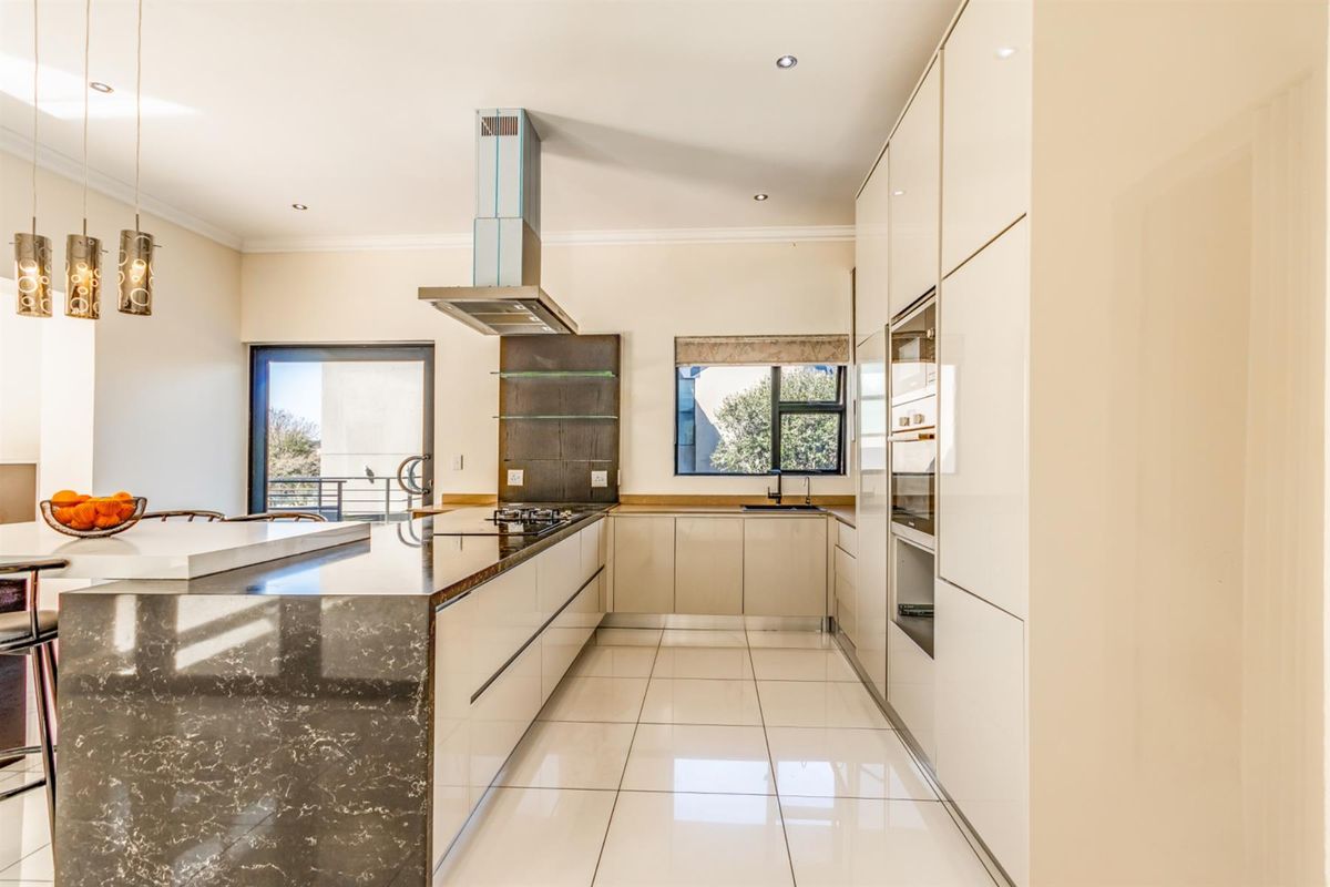 Modern kitchen featuring high-gloss cabinetry, stone countertops, a central island, built-in oven, and stainless steel extractor fan with tiled flooring.