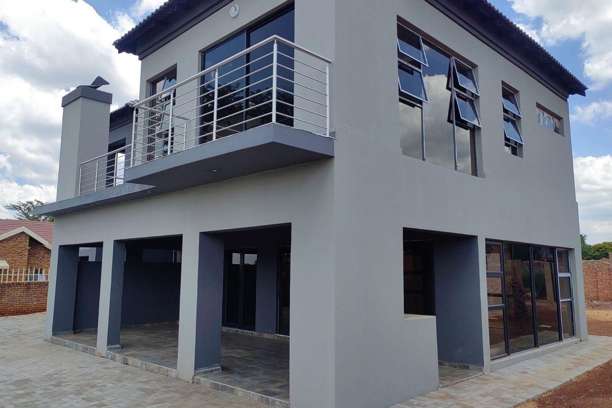 A modern double-story house featuring a covered ground-floor patio, a first-floor balcony with stainless steel railings, and large aluminum-framed windows.