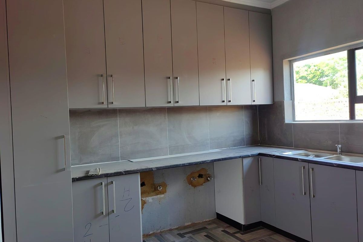 A kitchen area featuring grey cabinetry and a tiled backsplash, currently undergoing installation with exposed plumbing and unfinished wall sections.