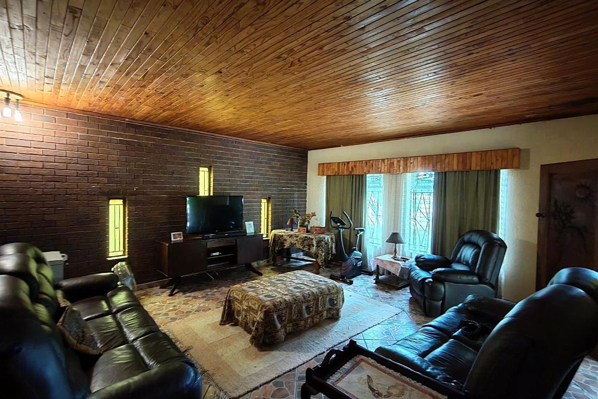 Spacious living room featuring a distinctive timber ceiling, exposed brick feature wall, and tiled flooring with natural light from vertical windows.