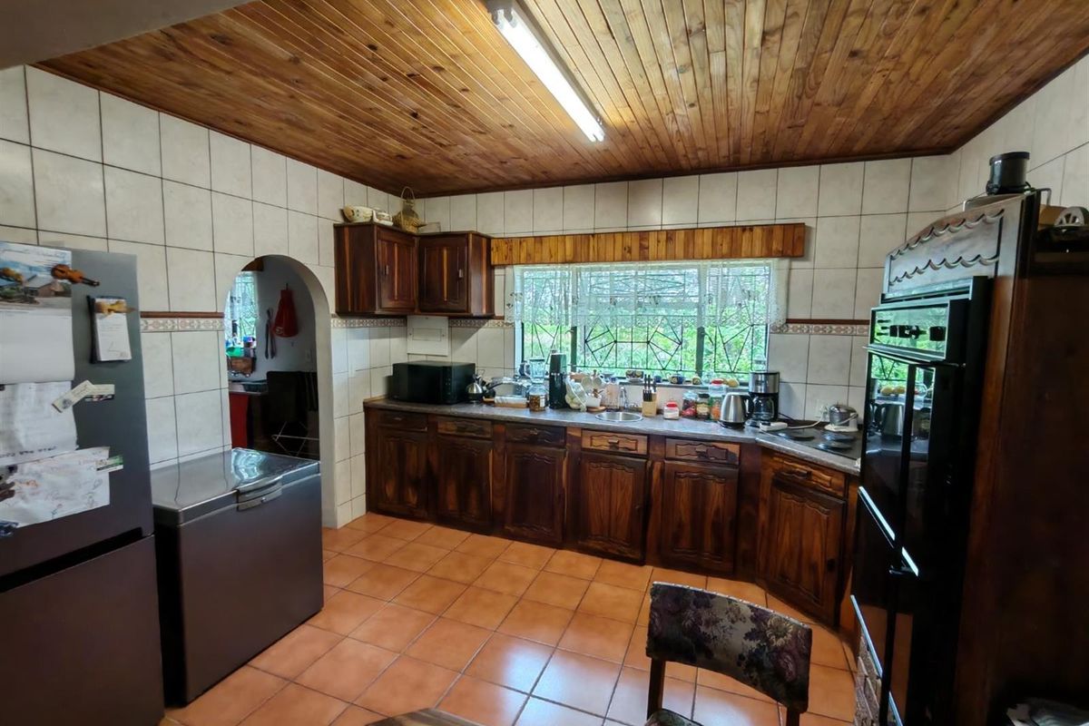 A functional kitchen featuring wooden cabinetry, tiled flooring, and a wooden ceiling, with an integrated oven and hob, offering a traditional aesthetic.
