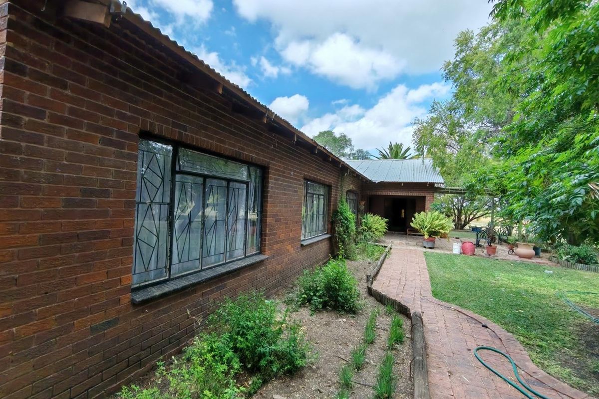 Rear view of a face brick small holding residence featuring a corrugated metal roof, steel-framed windows with security bars, and a brick-paved garden path.