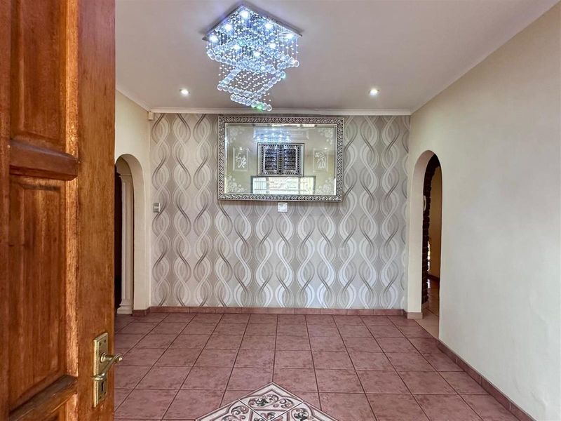An inviting entrance hall featuring tiled flooring, decorative wallpaper, and a modern crystal chandelier, providing a welcoming transition into the home.