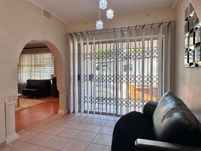 A living area featuring tiled flooring, an arched entryway, and a sliding glass door secured with a metal security gate.