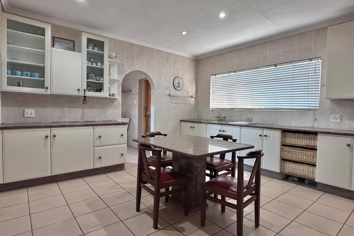 A functional kitchen featuring tiled flooring, ample cabinetry, stone-topped central island, and integrated sink, with an adjacent arched doorway leading to a utility area.