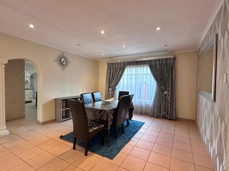 A spacious dining room featuring tiled flooring, recessed downlighting, and an arched entryway leading to the kitchen area.