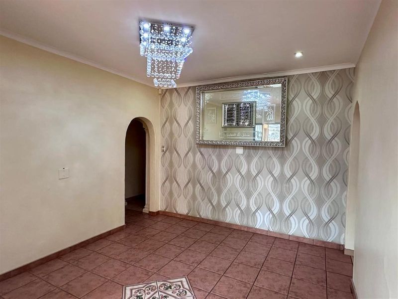 A well-maintained living area featuring decorative wallpaper, tiled flooring, an arched doorway, and a modern crystal chandelier.