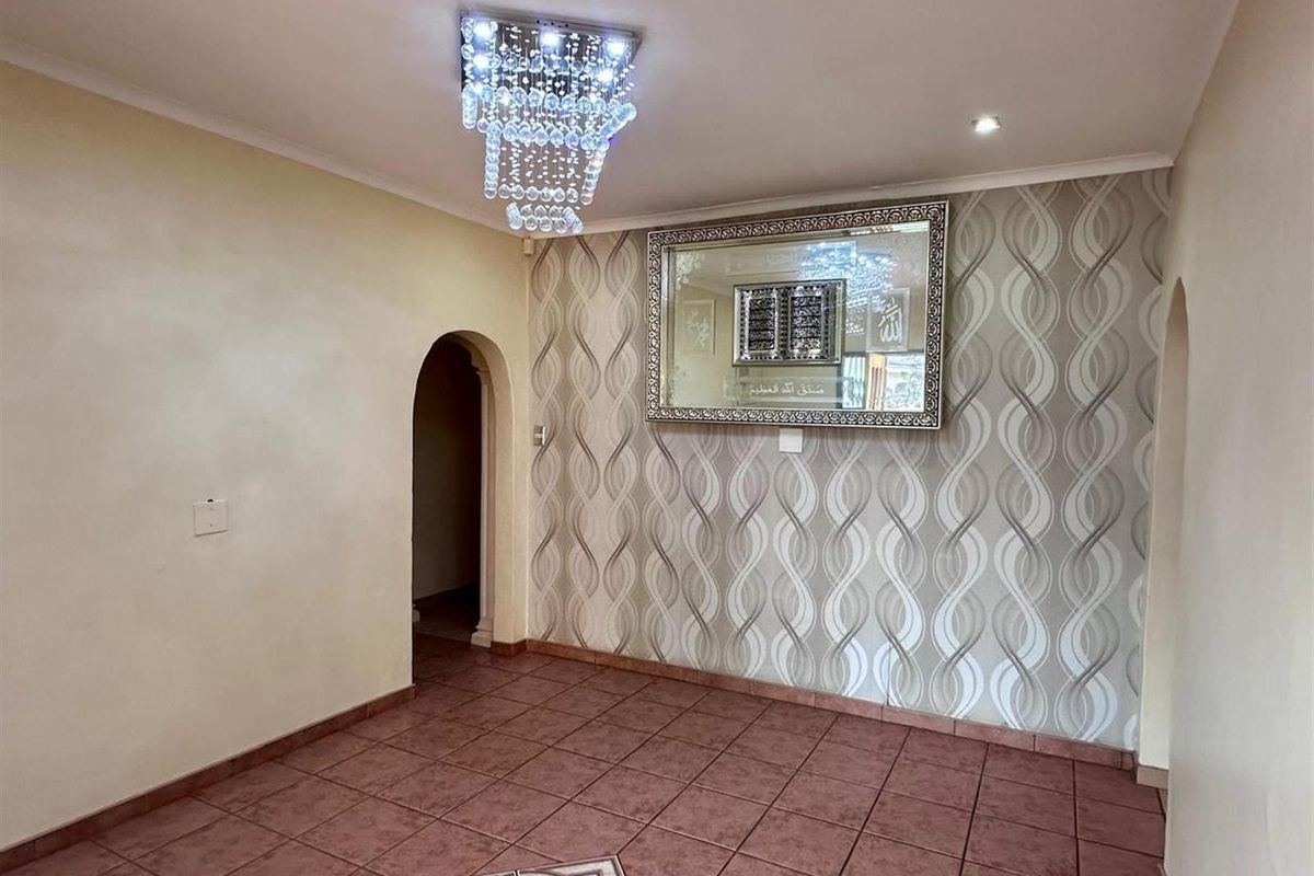 A well-maintained living area featuring decorative wallpaper, tiled flooring, an arched doorway, and a modern crystal chandelier.