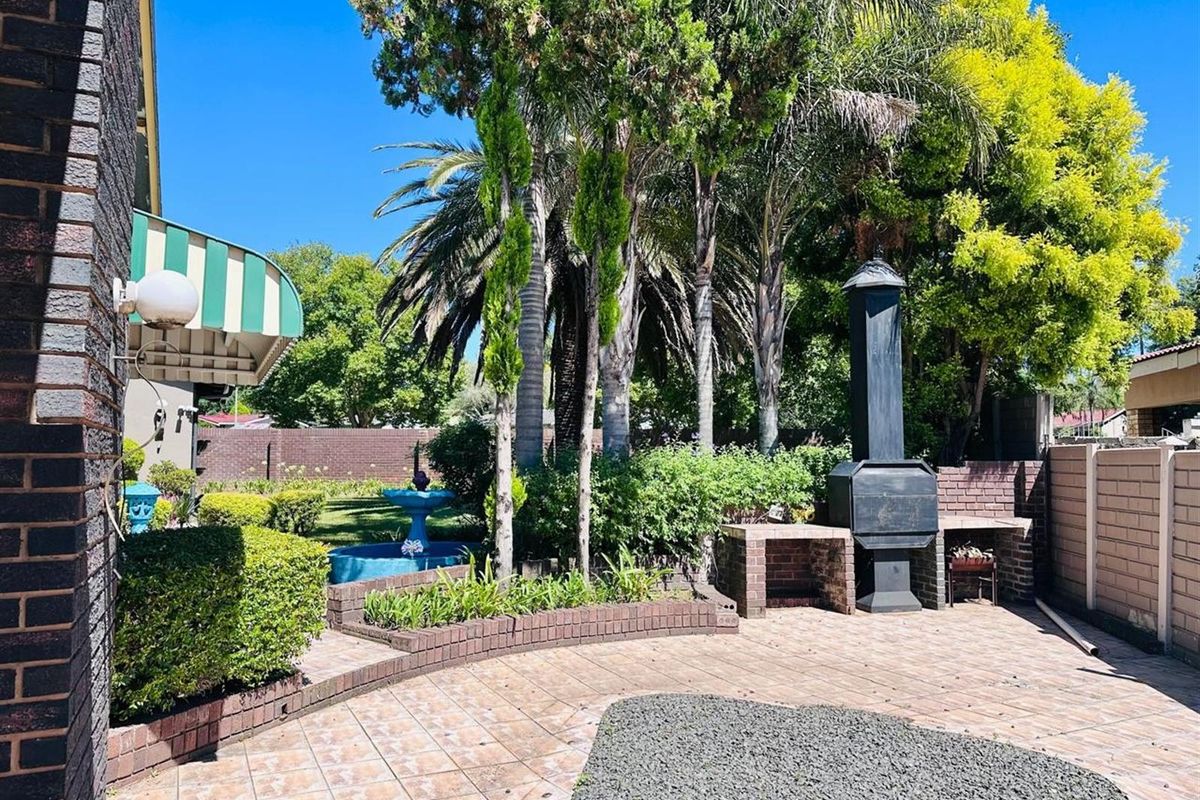 A private rear garden featuring a paved patio area with a built-in brick braai, established landscaping, and a decorative water feature.
