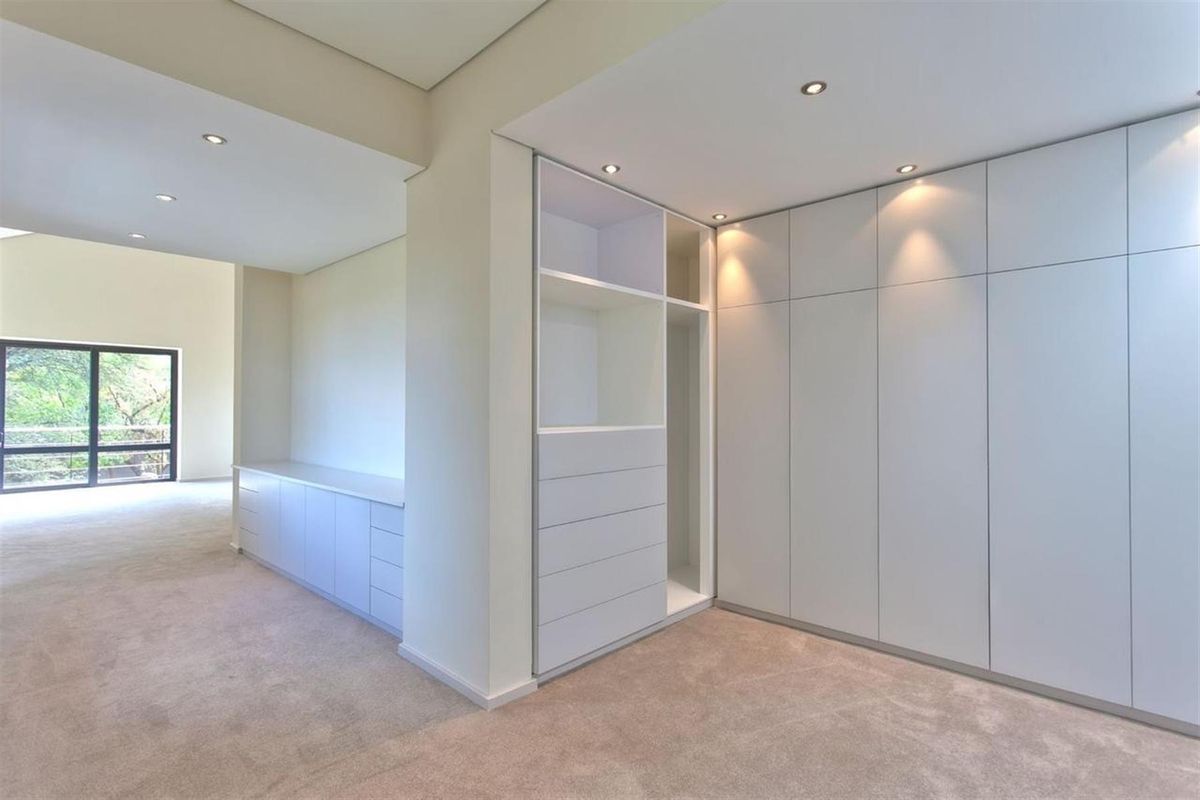 Spacious bedroom featuring extensive built-in cabinetry, integrated storage solutions, recessed downlighting, and neutral carpeting throughout.