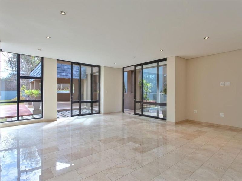Spacious, light-filled living area featuring polished stone flooring, recessed downlighting, and large floor-to-ceiling glass sliding doors opening onto an outdoor patio.