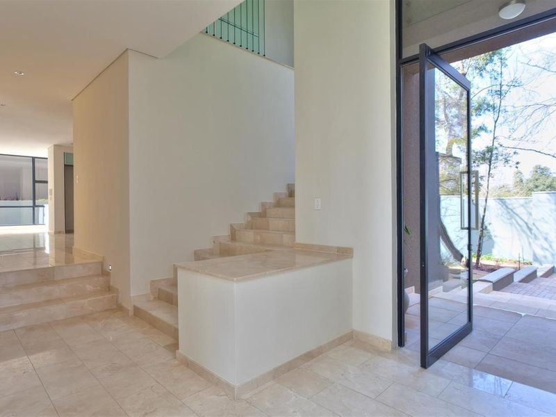 Spacious modern entry hall featuring polished stone flooring, a grand staircase, and a large glass pivot door leading to the exterior.