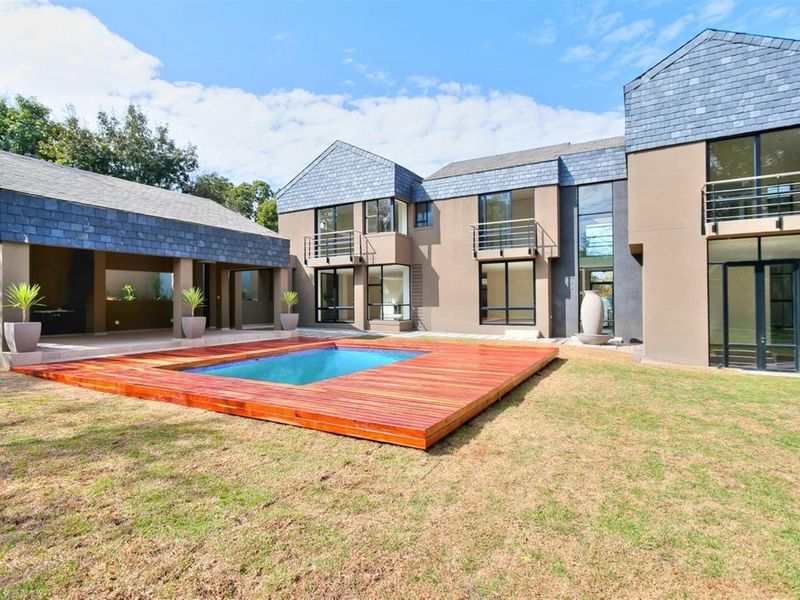 Spacious rear exterior view featuring a modern multi-level home, a swimming pool with timber decking, and a covered patio area.