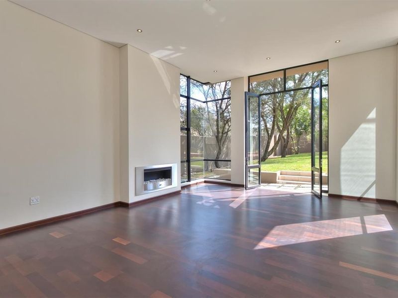 Spacious living room featuring dark hardwood flooring, a modern built-in fireplace, and floor-to-ceiling windows with direct access to the garden.