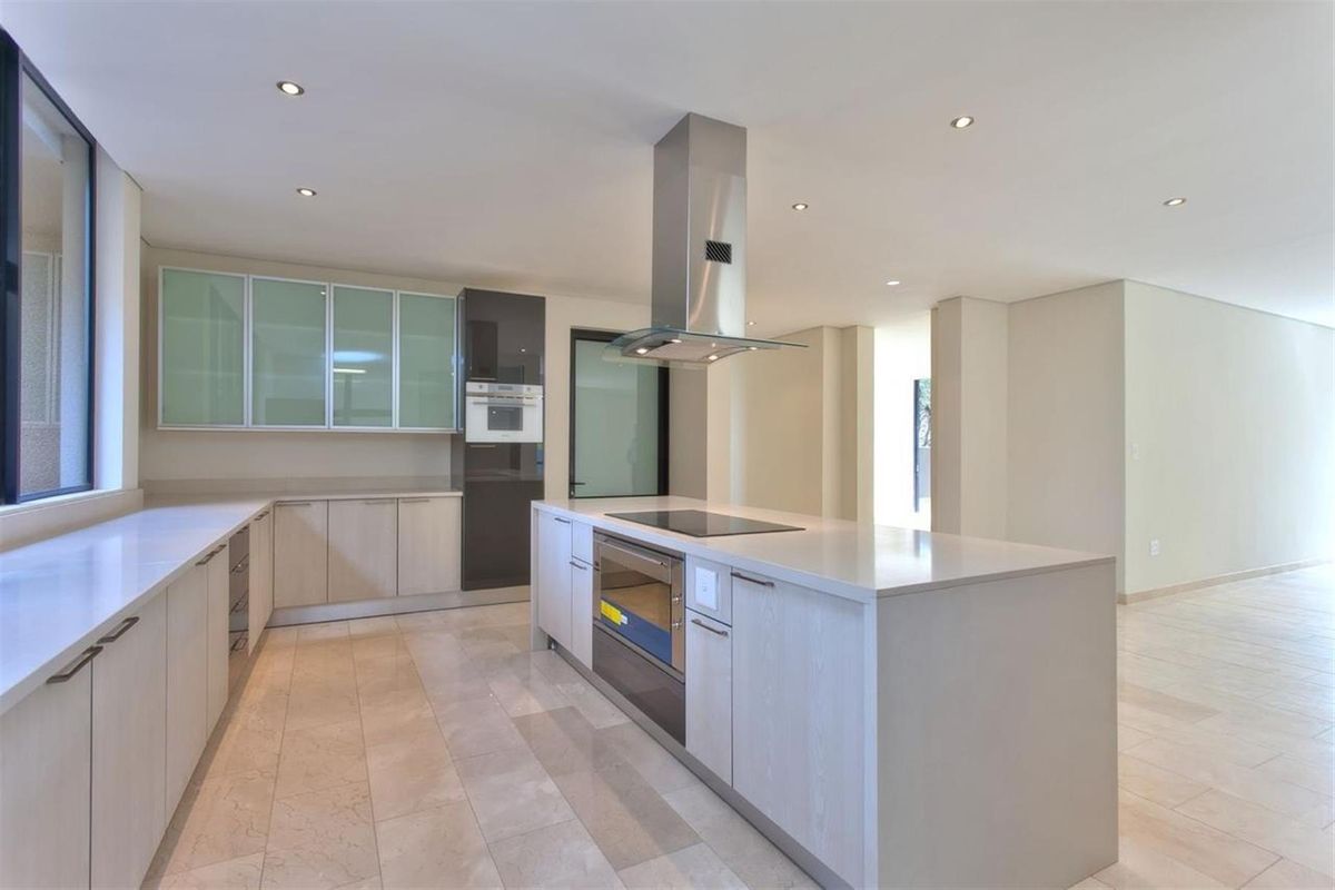 Modern kitchen featuring a central island with a built-in cooktop and oven, stainless steel extractor fan, and sleek cabinetry with stone countertops.