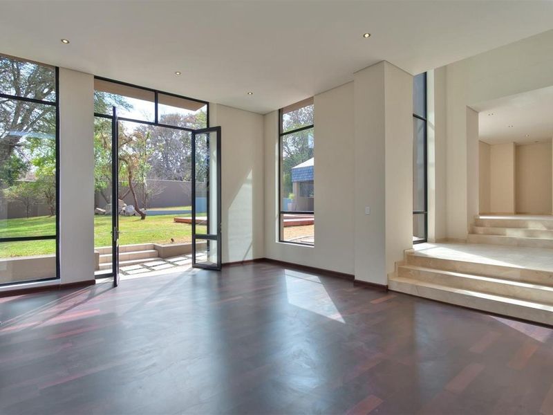 Spacious living area featuring dark hardwood flooring, floor-to-ceiling windows, recessed lighting, and direct access to the rear garden through large glass doors.