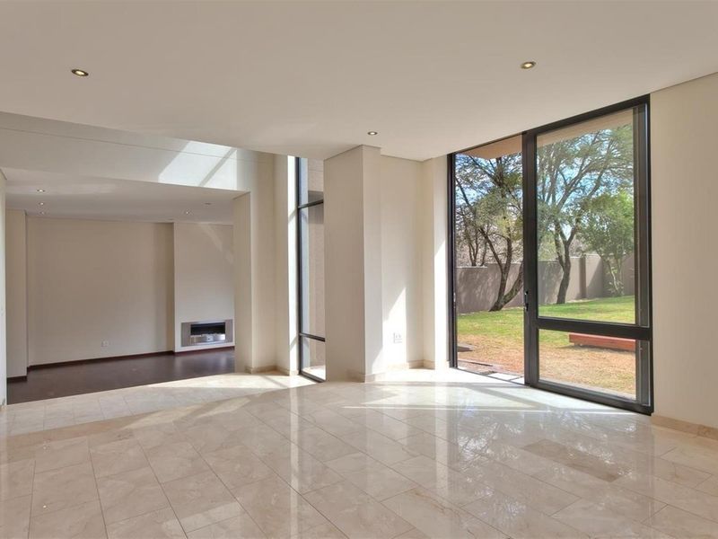 Spacious open-plan living area featuring polished stone flooring, recessed downlighting, a modern built-in fireplace, and large floor-to-ceiling windows overlooking the garden.