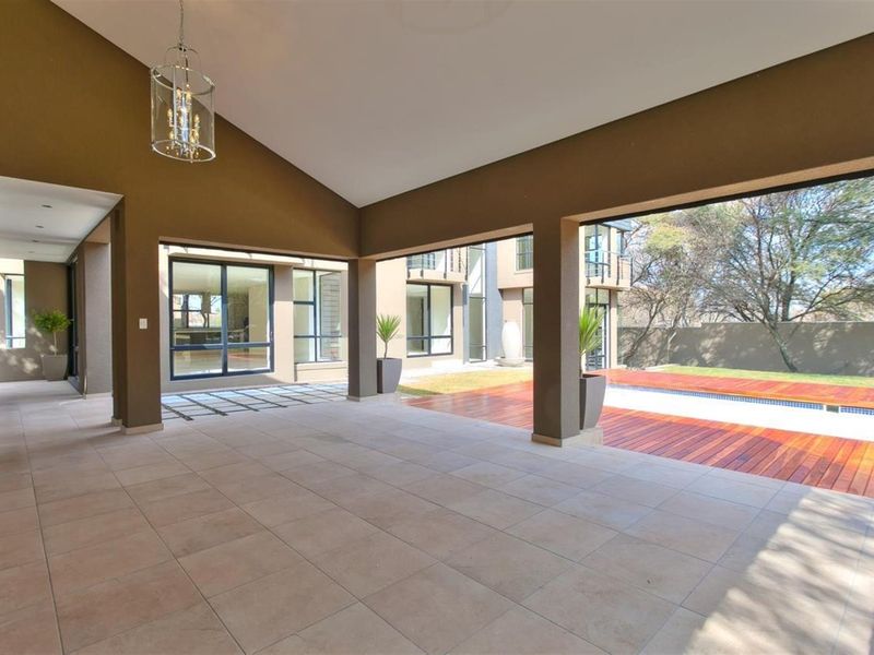 Spacious covered patio featuring tiled flooring, high ceilings, and seamless flow to the outdoor pool area and wooden decking.