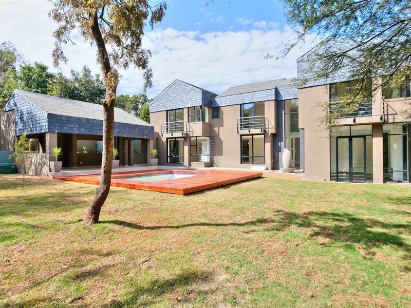 Spacious rear exterior view featuring a modern multi-level residence, a swimming pool with timber decking, and a covered patio area set within a garden.
