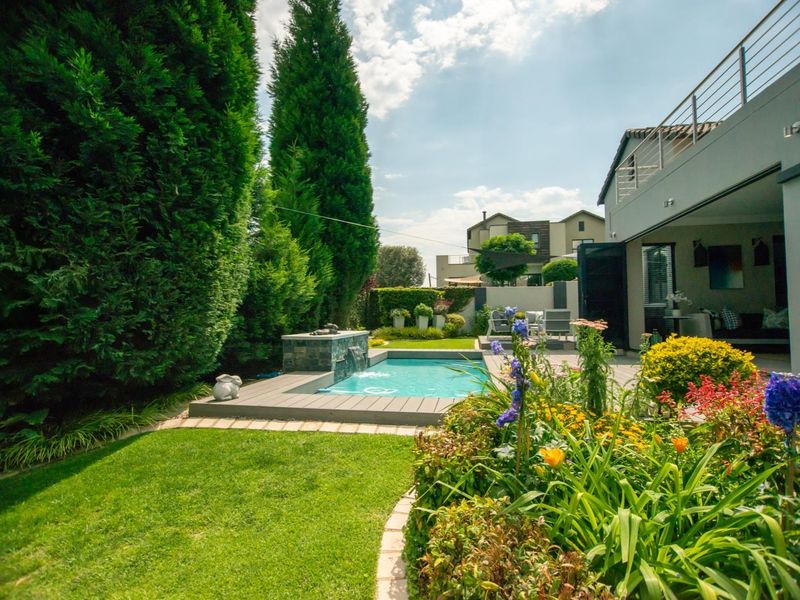A well-maintained rear garden featuring a swimming pool with a built-in water feature, timber decking, and established landscaping.
