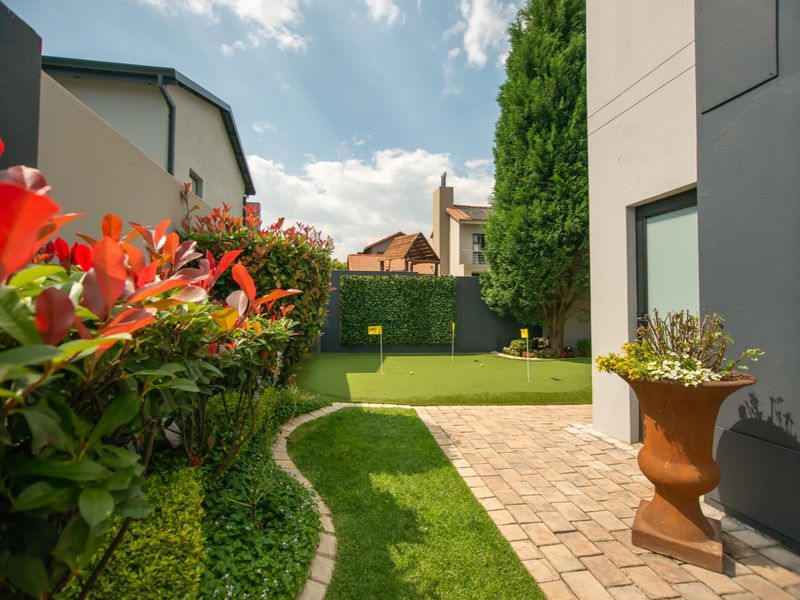 A well-maintained rear garden featuring a private putting green, paved walkway, and manicured landscaping.