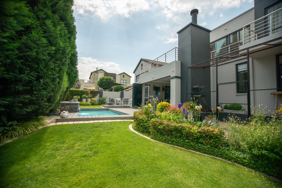 A well-maintained rear garden featuring a swimming pool, wooden decking, an outdoor fireplace, and a balcony overlooking the landscaped yard.