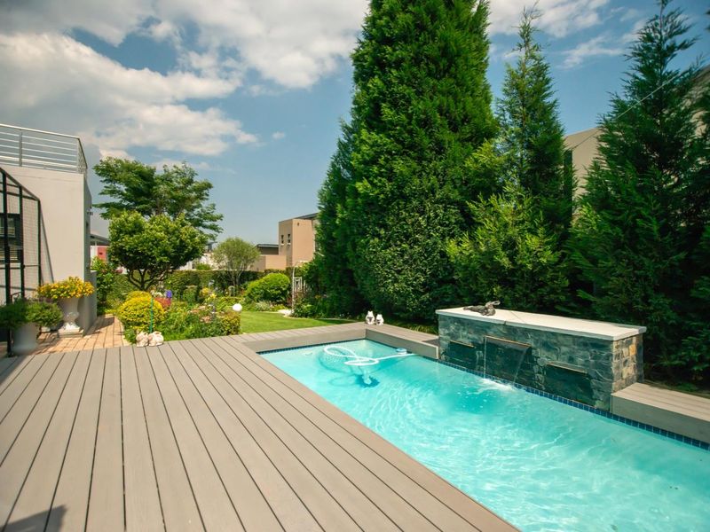 A well-maintained outdoor pool area featuring composite decking, a stone water feature, and a landscaped garden with mature trees.