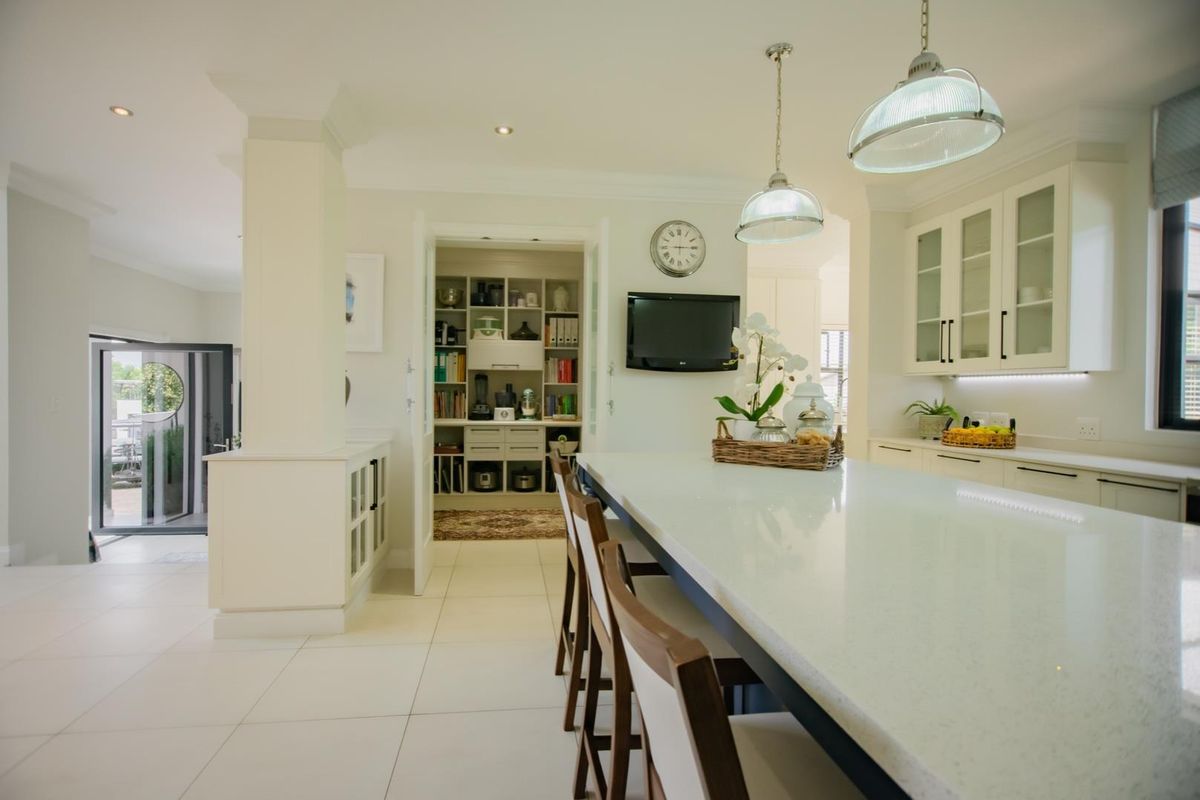 Modern kitchen featuring a large central island with stone countertops, ample built-in cabinetry, pendant lighting, and an adjacent walk-in scullery area.