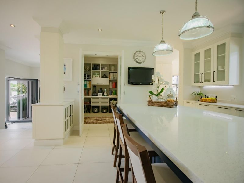 Modern kitchen featuring a large central island with stone countertops, ample built-in cabinetry, pendant lighting, and an adjacent walk-in scullery area.