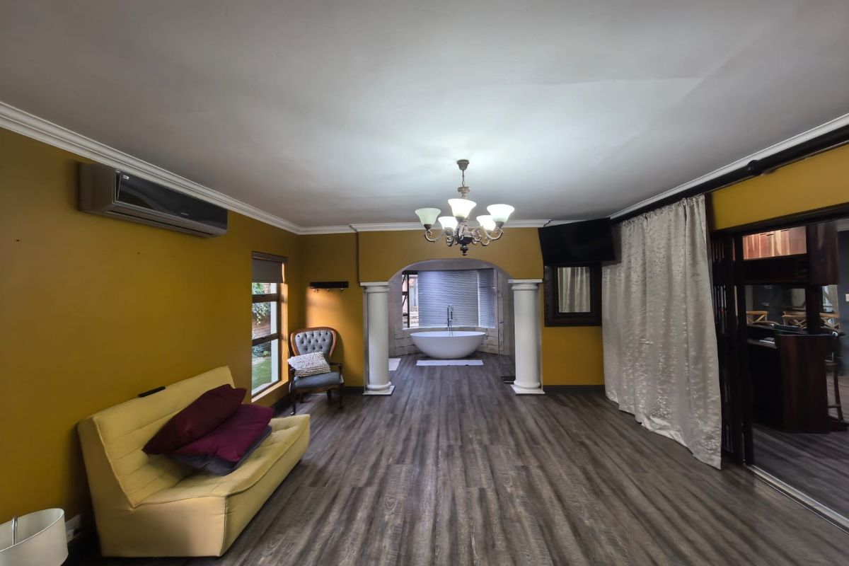 Spacious bedroom featuring laminate flooring, a central archway with decorative columns, and an integrated ensuite area with a freestanding bathtub.