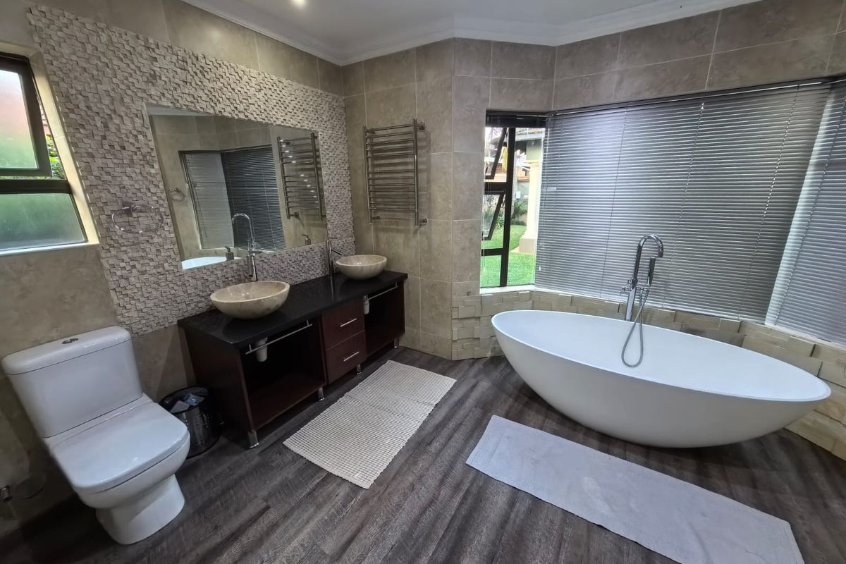 Modern bathroom featuring a freestanding bathtub, double vanity with vessel sinks, heated towel rail, and neutral tiled finishes.