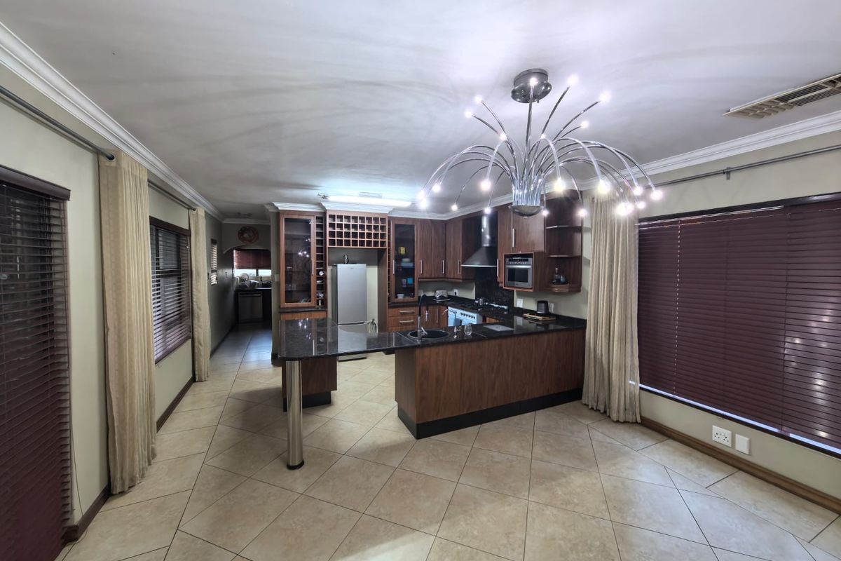 Spacious kitchen featuring dark wood cabinetry, granite countertops, a central island, and integrated appliances, finished with ceramic floor tiles and decorative lighting.