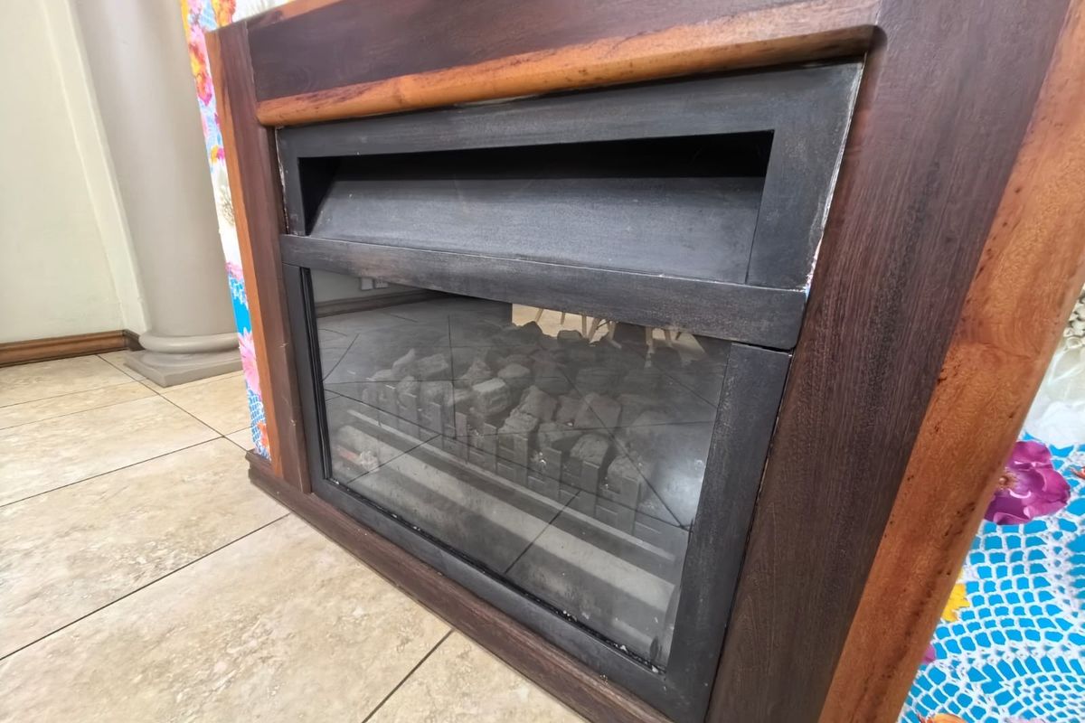 A close-up view of a built-in fireplace with a wooden surround and ceramic tiled flooring in a living area.
