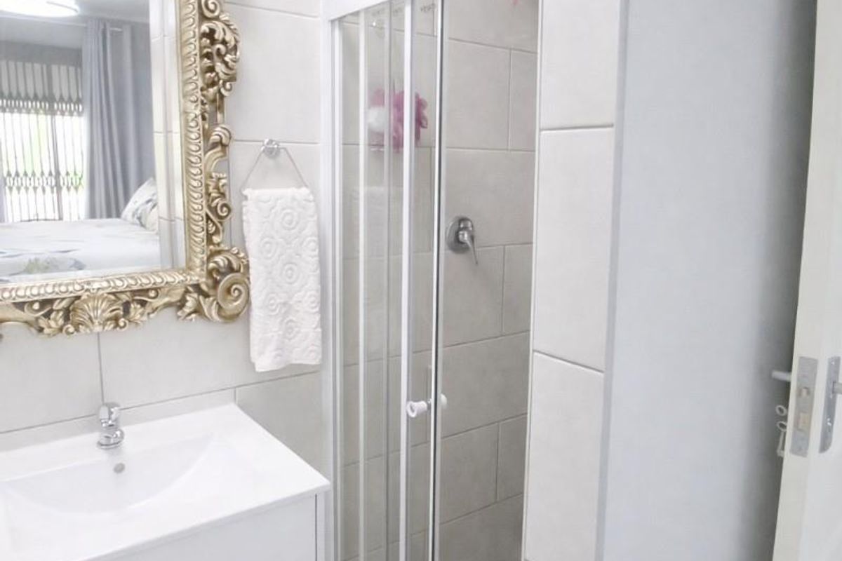 Modern bathroom featuring a white vanity cabinet, basin, and a glass-enclosed shower with neutral wall and floor tiling.
