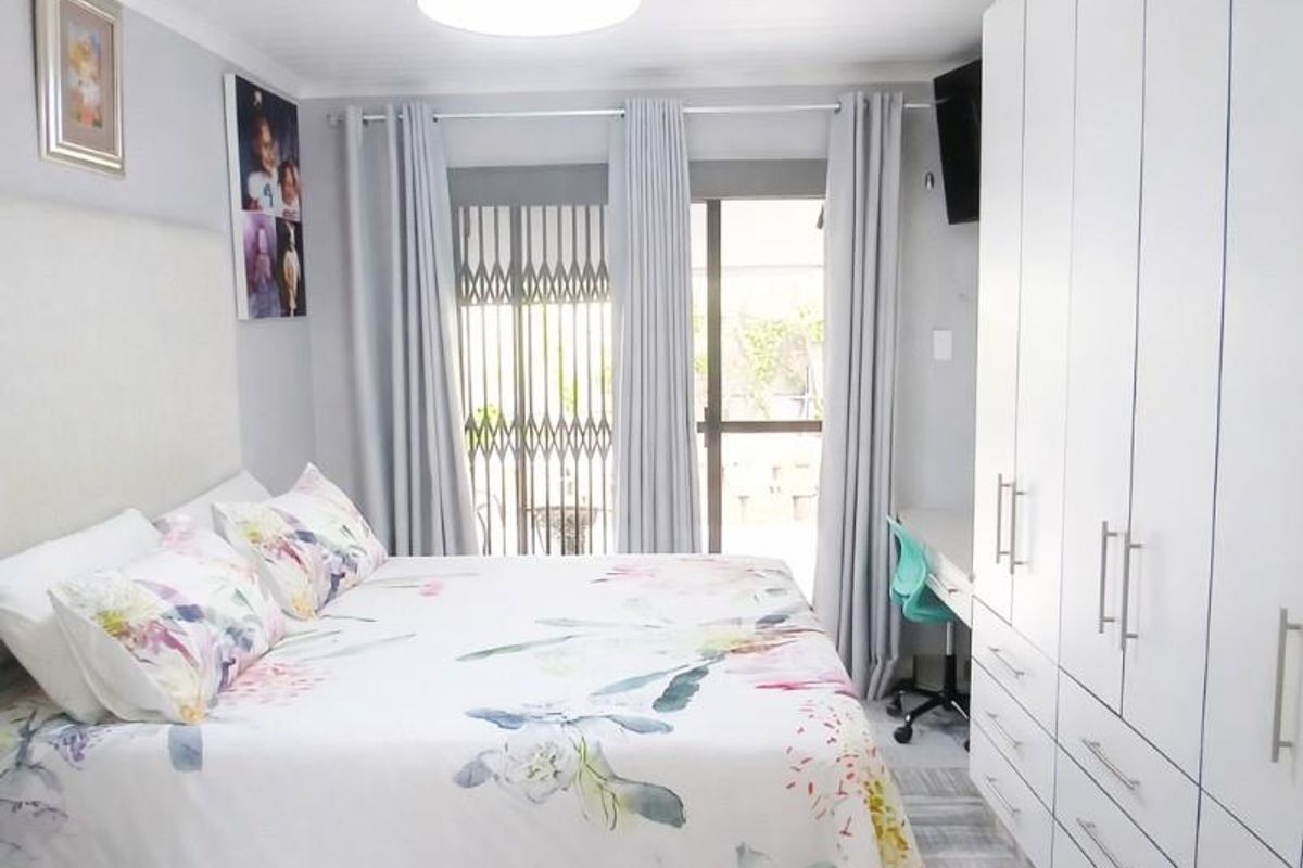 A well-maintained bedroom featuring built-in cupboards, a ceiling fan, tiled flooring, and direct access to the outdoors via a sliding door with security gate.