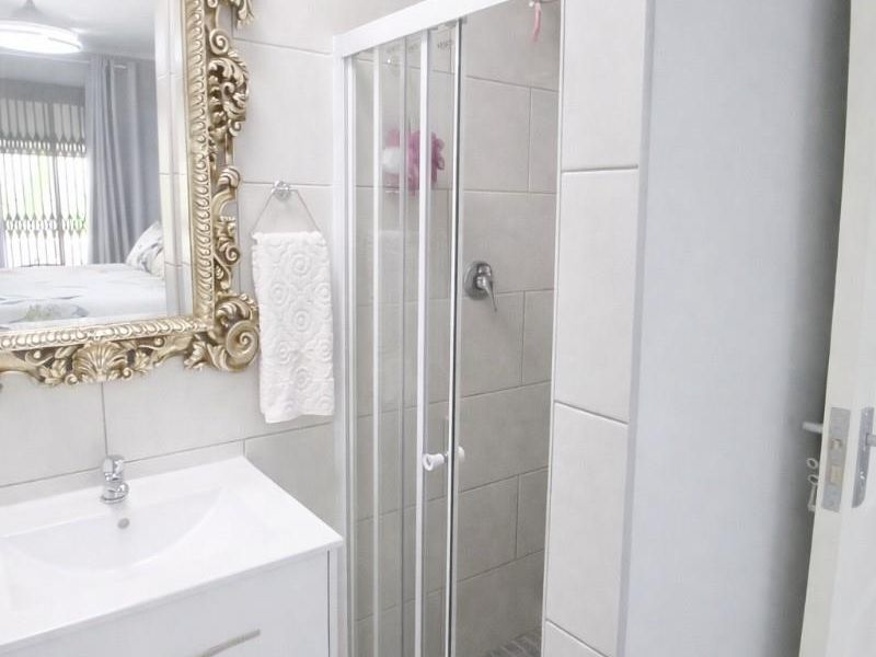 Modern bathroom featuring a white vanity cabinet, basin, and a glass-enclosed shower with neutral wall and floor tiling.