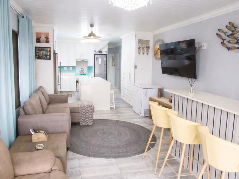 Open-plan living and kitchen area featuring a central island, breakfast bar, modern tiled flooring, and a bright, neutral aesthetic.