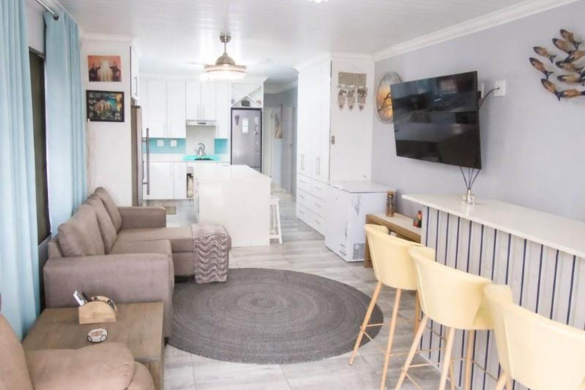 Open-plan living and kitchen area featuring a central island, breakfast bar, modern tiled flooring, and a bright, neutral aesthetic.