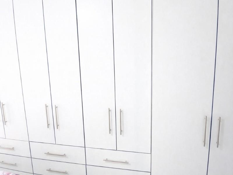 A bright bedroom featuring extensive floor-to-ceiling built-in white cabinetry with modern hardware and contemporary wood-look tiled flooring.
