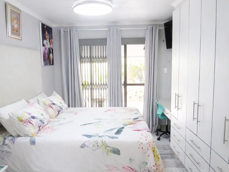 A well-maintained bedroom featuring built-in cupboards, a ceiling fan, tiled flooring, and direct access to the outdoors via a sliding door with security gate.
