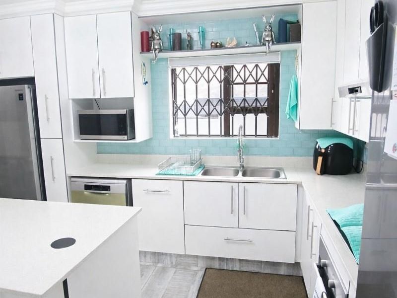 Modern kitchen featuring white cabinetry, stone countertops, a central island, and a light blue tiled splashback with integrated appliances.