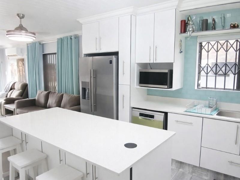 Modern open-plan kitchen featuring a central island, white cabinetry, quartz countertops, and integrated appliances, seamlessly flowing into the adjacent living area.