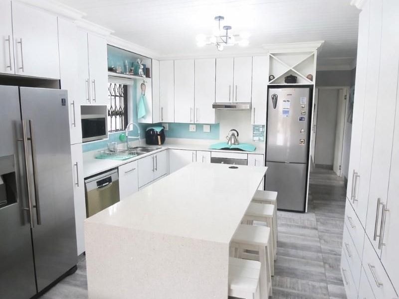 Modern kitchen featuring white cabinetry, a central quartz island, stainless steel appliances, and light-toned tiled flooring with a clean, contemporary aesthetic.