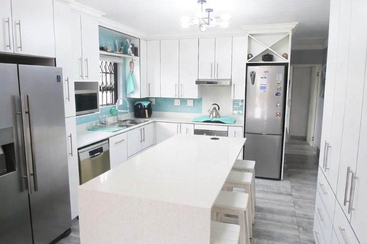 Modern kitchen featuring white cabinetry, a central quartz island, stainless steel appliances, and light-toned tiled flooring with a clean, contemporary aesthetic.