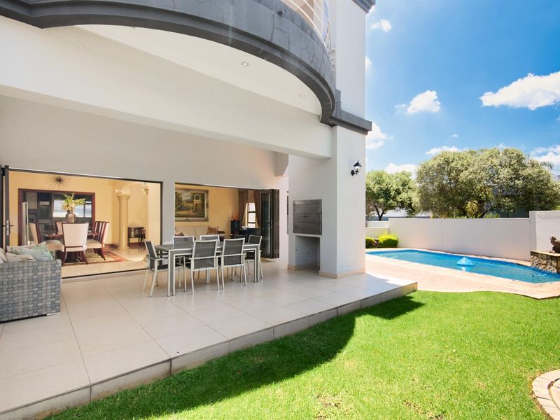 Covered patio area featuring built-in braai, tiled flooring, and seamless flow to the swimming pool and landscaped garden.