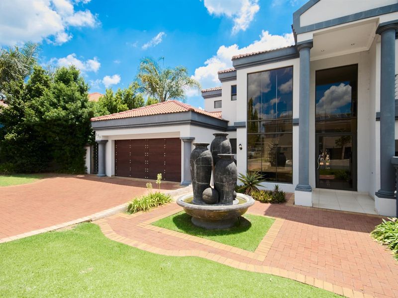 A well-maintained front exterior featuring a paved driveway, double garage, double-volume glass facade, and a decorative water feature in the landscaped garden.
